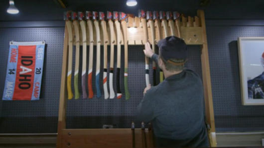 A photo of a man placing some axes on a stand. Each axe has a different colored and styled handle.