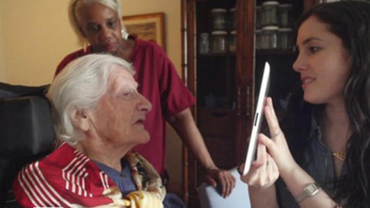 A photo of a woman showing something on a tablet to an older woman, while a third person is watching.