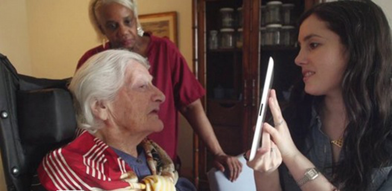 A photo of a woman showing something on a tablet to an older woman, while a third person is watching.