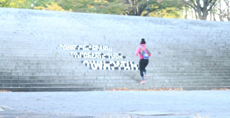 A photo of a person wearing a pink blouse and climbing on some stairs. The stairs have on them some text but the angle of view is not clear to understand it.