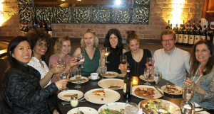 A photo of a group of people sitting at a restaurant table, each having a glass in their hand and toasting.