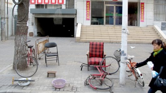 A photo of a sidewalk with chairs, bicycle tires, bicycle pumps and bicycles in front of a building that has Asian writings on it.