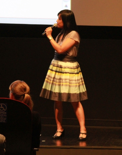 A photo of a woman wearing a yellow dress and giving a lecture on the stage.