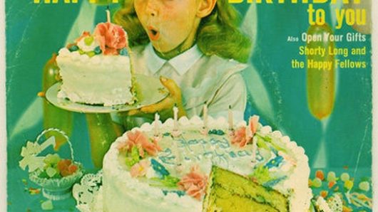 A photo of an old birthday cake commercial showing a girl holding a piece of cake and the rest of the it surrounded by jelly fruits.