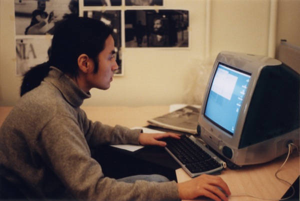A photo of a man siting at a desk and working on an old pc.