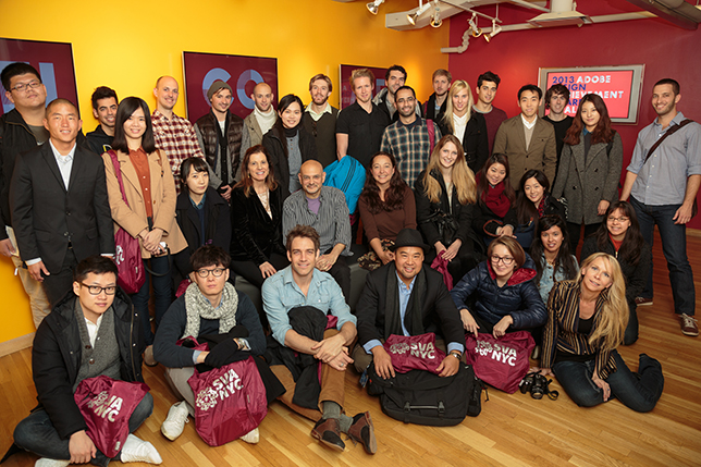 A photo of a group of people sitting and standing in an art gallery while having burgundy colored bags with SVA NYC logo on them.