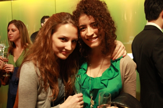 A photo of two girls among other people and in the background is a green wall.