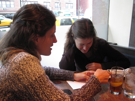 A photo of two women showing one another something on the table.