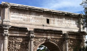 A side of an old roman stone arch with some text engraved on it.