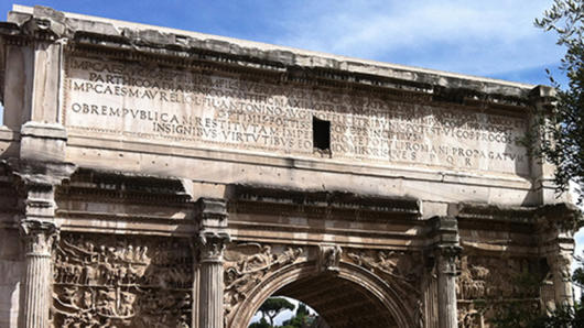 A side of an old roman stone arch with some text engraved on it.