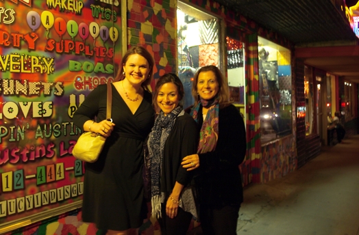 A photo of three women standing in front of a colorful wallpaper.