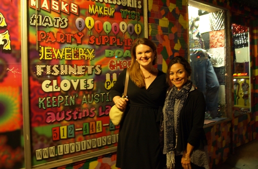 A photo of two women standing in front of a colorful wallpaper.
