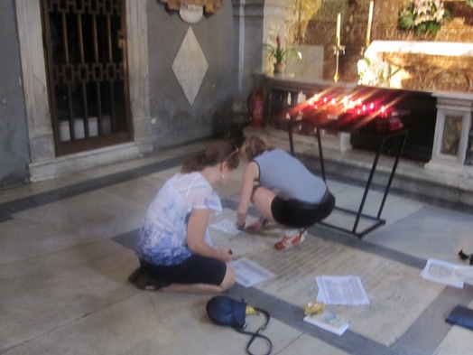 A photo of two girls trying to copy some stone engravings.