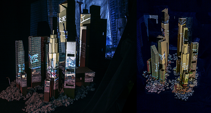 A photo of an art exhibit that show what looks like a cardboard city scape with lights.