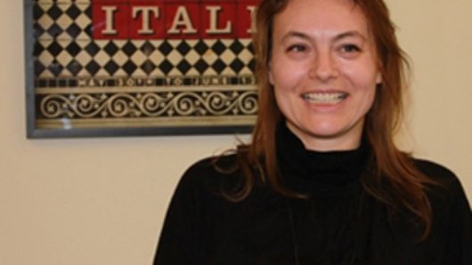 A photo of a smiling woman in front of a black and white checkered board with the words DESIGN ITALY in red squares.