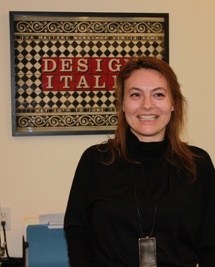 A photo of a smiling woman in front of a black and white checkered board with the words DESIGN ITALY in red squares.