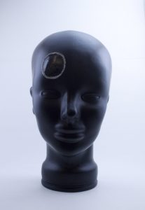 A human head made from black rubber with a black rock on its head.
