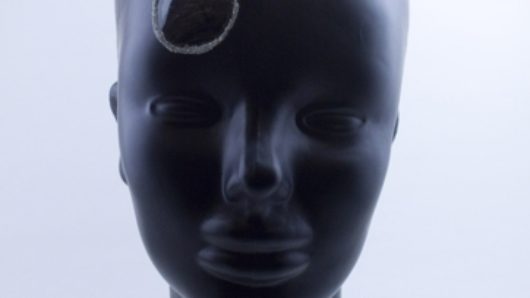 A human head made from black rubber with a black rock on its head.