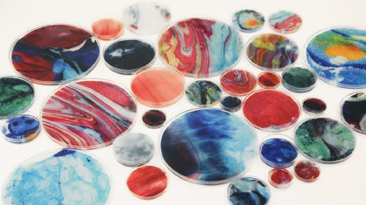 Colorful white, green, red, blue and yellow resin art put in different petri dishes.