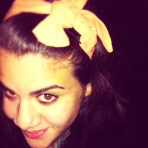 A photo of a woman wearing a yellow bow on her head.