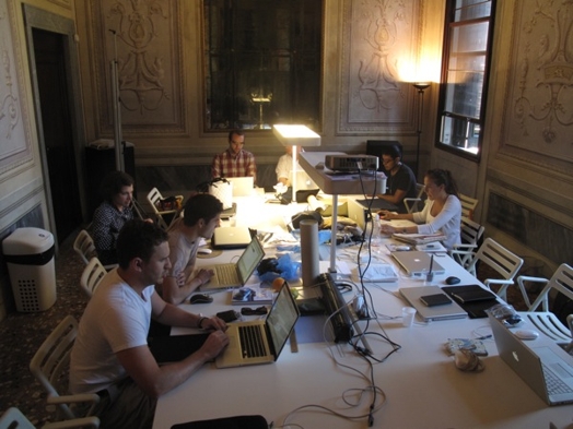 A photo of a group of people sitting around a table and working on their laptops.