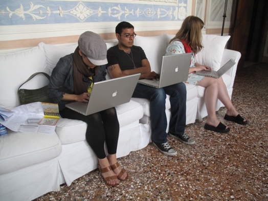 A photo of three people sitting on a couch while each working at laptops.