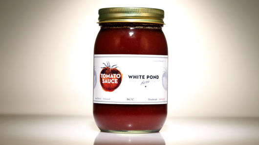 A glass jar filled with tomato sauce and a label with a tomato on it and the text White Pond.