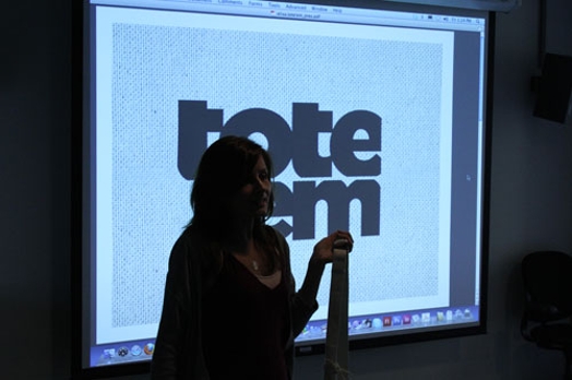 A photo of a woman giving a lecture while standing in front of a screen projector.