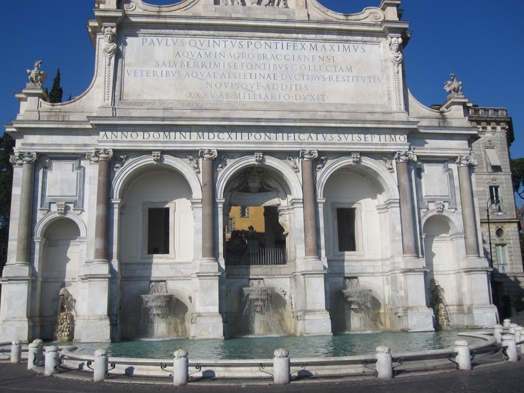 A photo of a stone building with pillars, a fountain on the front and some engravings on it.