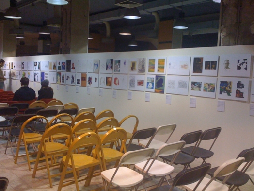 A photo of a room with chairs and an improvised wall with different art pieces on it.