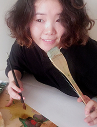 A photo of a woman smiling an holding some paint brushes in her hands.