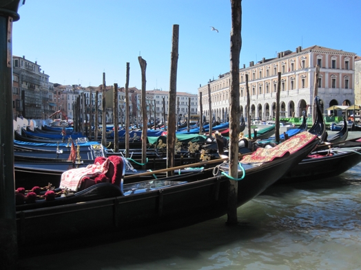 A photo of some covered gondolas sitting in a water canal near a square.