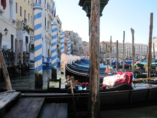 A photo of some covered gondolas sitting in a water canal near a square.