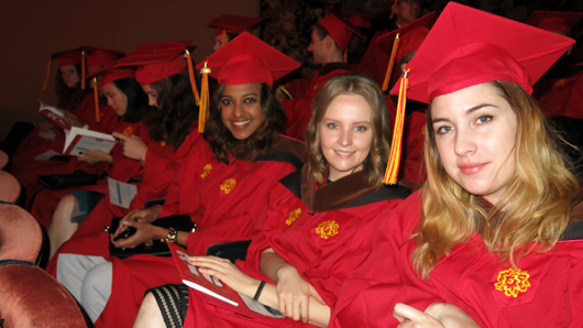 A group of grad students wearing red SVA robes and hats with gold yellow logos of the school.