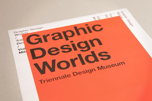 A photo of apiece of white and orange paper with the text: Graphic Design Worlds Triennale Design Museum.