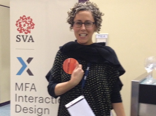 A photo of a woman holding a red cardboard circle while standing behind an SVA MFA Interactive Design banner.