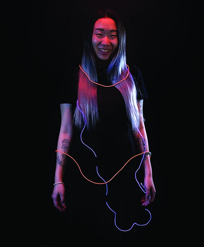 A smiling girl with a florescent blue and red wires around her.