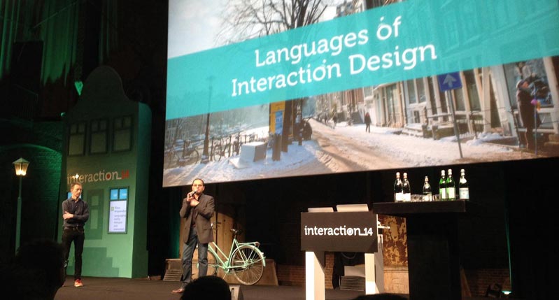 A photo of a person giving a lecture and showing a city street on a projector screen. The title over the image is: Languages Of Interaction Design.