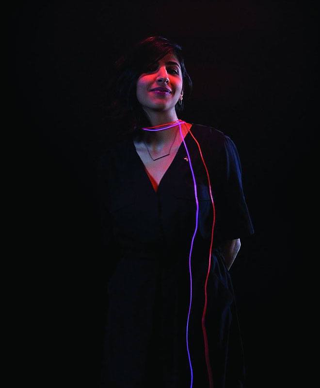 A smiling girl with red and blue glowing wires around her neck.