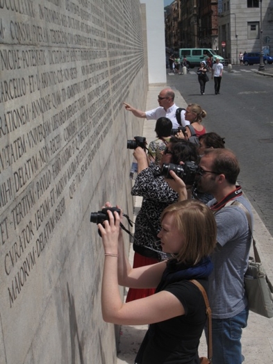 A group of people taking pictures and looking at an engraved stone wall.