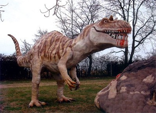 A photo of a dinosaur sculpture with blood spilling from his mouth while near it there is another sculpted creature.