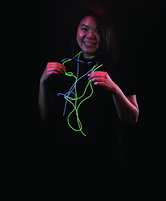 A smiling girl with blue and green glowing wires around her.