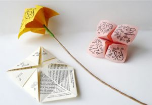 A photo of chatterboxes paper games, one made to look like a yellow and green flower, the others white and pink colored.