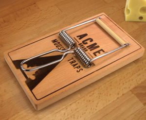 A wooden mouse trap with engraved text: Acme Brand Mouse Traps.