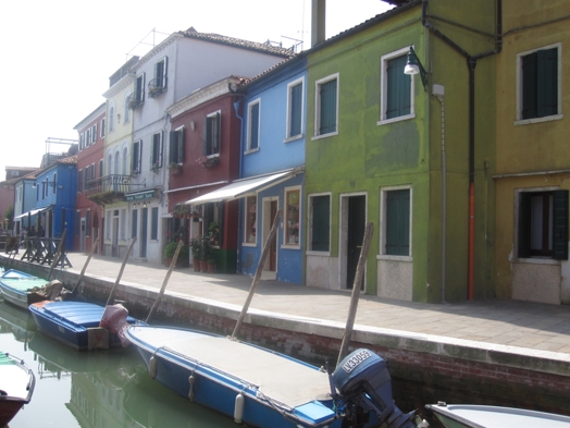 A photo of some colored houses and some covered boats sitting in a water canal.
