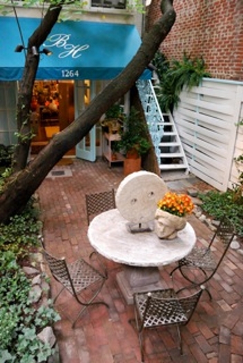 A photo of a terrace with a white table and four chairs. On the table there is a stone wheel and a stone head that holds flowers.