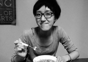 A black and white photo of a woman wearing glasses and eating some pasta.