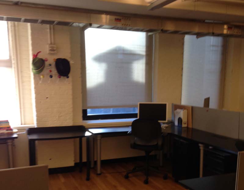 A  photo of a desk wit a pc on it. Behind there is a screen with a shadow of a man wearing a graduation robe and hat.