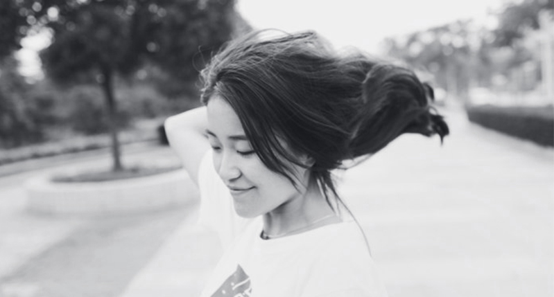 A black and white photo of a girl standing in the street with her hair in the wind.