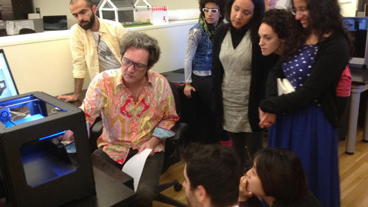A photo showing a professor teaching some students how to work with a 3d printer.